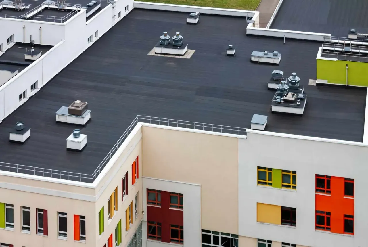 Aerial view of a modern school building with a black roof, white walls, and colorful window panels.