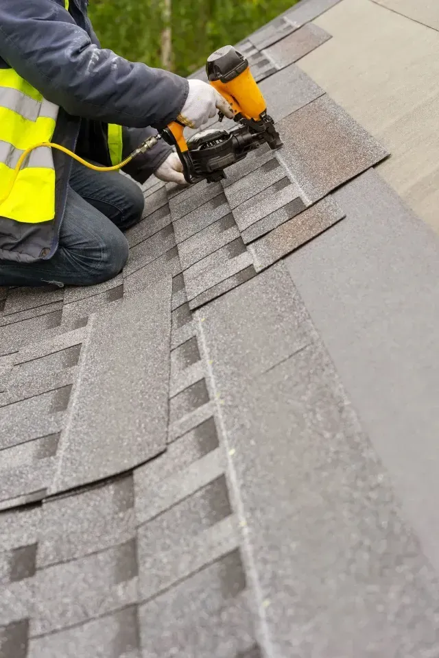 Roofing company installing shingles with a nail gun on a sloped roof in Aurora, IL.
