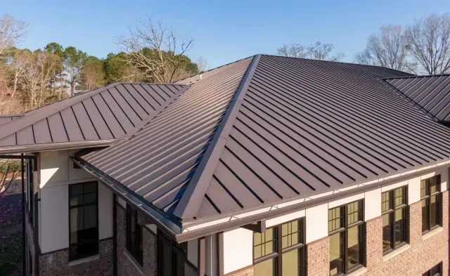 An aerial view of a dark-colored metal standing-seam roof on a modern building with brick and stucco siding.